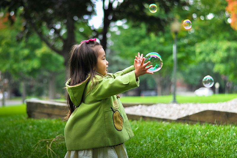 Child catching a bubble in a park